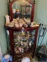 Front view of curved glass china cabinet showing clarity of glass, wood framing, and mirrored top with bevelled edges.
