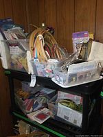 Overall view of two upper shelves containing multiple bins with craft supplies including yarn, wooden hoops, patterns, ribbons, and other materials.
