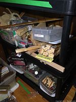 Photo of black shelving unit with plastic bins holding craft items including wood shapes, buttons, marbleizing kit box, and ribbon bundles