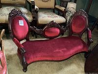 Full view of Victorian style doll sofa showing overall design, red velveteen upholstery, and carved wooden frame with claw feet.