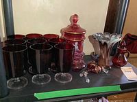 Overview of ruby glass cups, cranberry jars, art glass vases, and red glass Avon jar on display surface