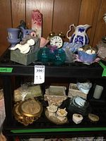 Wide view showing an assortment of home decor items including porcelain pitcher, vases, candles, and clock arranged on a black table against wood paneling.