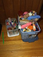 Three plastic totes filled with colorful yarn skeins, knitting needles, scissors, and other knitting supplies.