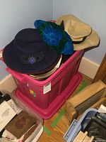 Photo showing pink tote filled with various vintage ladies hats of different materials and colors including felt and velvet, with informational sticker visible on tote.