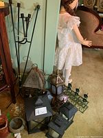 View of entire lot showing various lanterns and candle holders grouped on the floor against a wall, including the tall black metal candle holder, green wall-mounted candelabra, and multiple metal lanterns in different shapes and sizes.