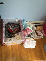 Photo of three plastic bins on the floor filled with assorted linens, doilies, embroidered pieces, napkins, and fabric handkerchiefs.