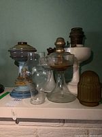 Overview of seven oil lamp bases and several glass shades including milk glass and frosted glass shades.