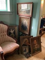 Group of all framed prints leaning against wall beside upholstered chair