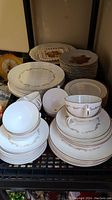 Full lot display showing stacked Royal Doulton dinnerware with gold floral scroll trim, Johnson Bros. patterned plates in the back.