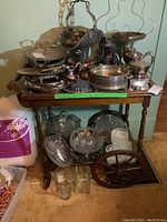 Front view of wood tea cart topped with various silver and glass serving pieces, showing cart and contents as displayed.