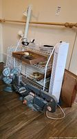 Wide angle image showing vintage Torcan metal fan, white wire shelving rack filled with tools and hardware, Craftsman orbital sander lying on floor, and tower fan standing tall to the right side.