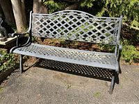 Front view of cast iron garden bench showing lattice design seat and floral patterned backrest under sunlight.