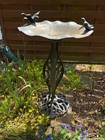 Front view of metal bird bath in garden showing scalloped basin with two bird figurines and ornate pedestal base