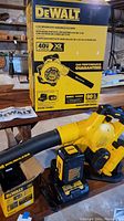DeWalt blower box showing model and features alongside the blower unit placed on wood surface with charger and battery visible.