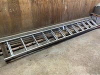 Full view of two aluminum ladder sections laying flat on the floor, showing approximate length and metal build.