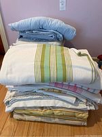Stack of folded flannel sheets with green stripes on white and blue solid sheets on top