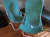 Two green and white striped outdoor sling style folding chairs shown from front, showing seats and metal frames.