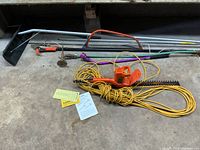 Overview of garden tool lot including hedge trimmer, sprinkler components, roof rake, pruner, and bow saw