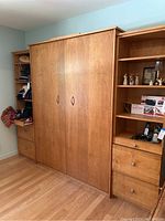 Closed Murphy bed flanked by left and right wood-tone shelving units