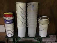 Overall view of stacks of plastic pails in white with metal handles and some lids