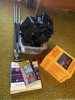 Photo of tripod, camera bags in plastic container, and photography books on floor