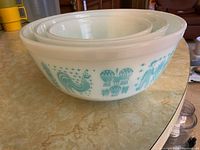 Front view of set of 3 nested Pyrex Butterprint mixing bowls showing turquoise farm motifs including roosters and corn on white glass.