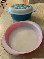 Horizon Blue oval covered casserole with lid on top and red shallow round casserole beneath it, shown on countertop.