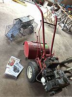 Overall front-right view of red Troy-Bilt tiller with owner’s manual on floor