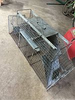 Large and smaller metal animal traps on concrete floor near bicycles and equipment, showing spring-loaded door mechanisms and metal trigger plates.