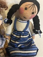 Close-up of crocheted doll showing black braided hair, blue and white crocheted clothing