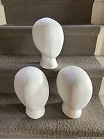 Three white Styrofoam head-shaped display sculptures arranged on carpeted steps, showing three-quarter front views of each.