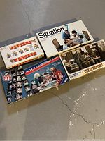 Photo showing the four vintage board games laid out on the floor; boxes visible include The VCR Quarterback Game, The Inventors, Situation 7, and Jitters.