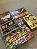 Photo showing six board games stacked partially, including The Muppet Show Chess, CSI The Senses, The Simpsons Clue, Bug-Opoly, Disney Scene It Game Pack, and Disney Trivia 2 tin.