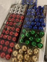 Six unopened boxes of shiny ball ornaments in red, blue, green, and gold colors, each box containing 24 ornaments.