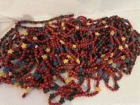 Close-up of tangled strands of red and green wooden bead garland with small colorful wooden stars and holly leaves scattered throughout.
