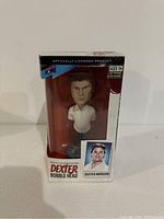 Front view of Dexter bobble head in original packaging with clear plastic window showing figure and facial details.