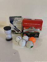 Photo of golf balls, golf swing-speed trainer box, Dunlop Spirit golf balls box, and a golf ball hourglass timer.