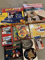 Photo of assorted boxed games including Space Magnet, Handimonium, Battleship card games, Pop Bead People, Team Up!, Mousie-Mousie shown on floor.