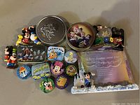 Top-down photo showing the full grouped display of Disney pins, tins, figurine, and framed photo.