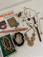 Overview of mixed jewelry laid out on a white surface showing variety of bracelets, necklaces, earrings, and a wristwatch.