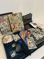 Wide view showing assorted stamps on sheets, stamp album, scissors, stamp tongs, bags of loose stamps, magnifier, and thematic sheets.