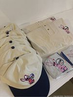 Seven off-white Energizer Bunny hats with navy blue brims arranged in a row next to the folded shirts and sealed beach balls.