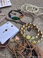 Photo of assorted bracelets including beaded and metal bangles along with a card of stud earrings on concrete surface.