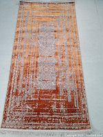 Full view of the rectangular machine made rug showing the warm copper background with intricate gray and white patterns and fringed edges.