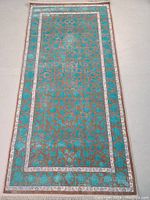Full view of the rectangular machine made rug showing the intricate raised pattern in turquoise and gray with a beige border.