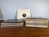 Two stacks of more than 20 vintage vinyl records on wooden tabletop.