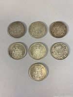 Seven Canadian silver 50 cent coins laid out showing coat of arms, showing wear and tarnish.