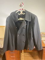 Black double-breasted wool and cashmere jacket hanging on a hanger, showing front view.