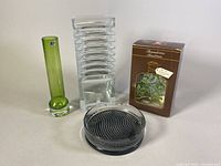 Four Scandinavian glassware items grouped together: a green vase, a ribbed clear glass Harmonikka vase, a round glass dish with swirl pattern, and a boxed item with botanical design on box.