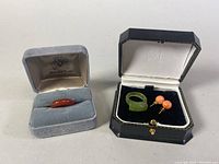 Two items in black jewelry box: two-toned green tourmaline ring and coral-colored pearl stud earrings.